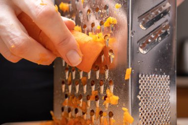 Kadın eli, haşlanmış havuçları yakın planda rendeleyiciye sürer. Yemek pişirmek.