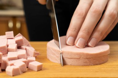 Kadın eli, yakın plan bir bıçakla kaynamış bir sosisi tahta bir tahtanın içinde küp haline getirdi..