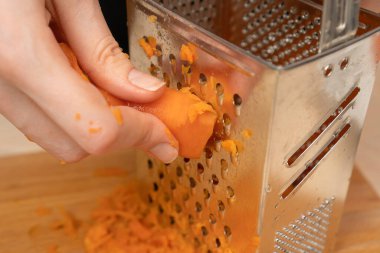 Kadın eli, haşlanmış havuçları yakın planda rendeleyiciye sürer. Yemek pişirmek.