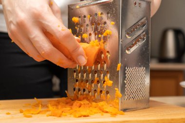 Kadın eli, haşlanmış havuçları yakın planda rendeleyiciye sürer. Yemek pişirmek.