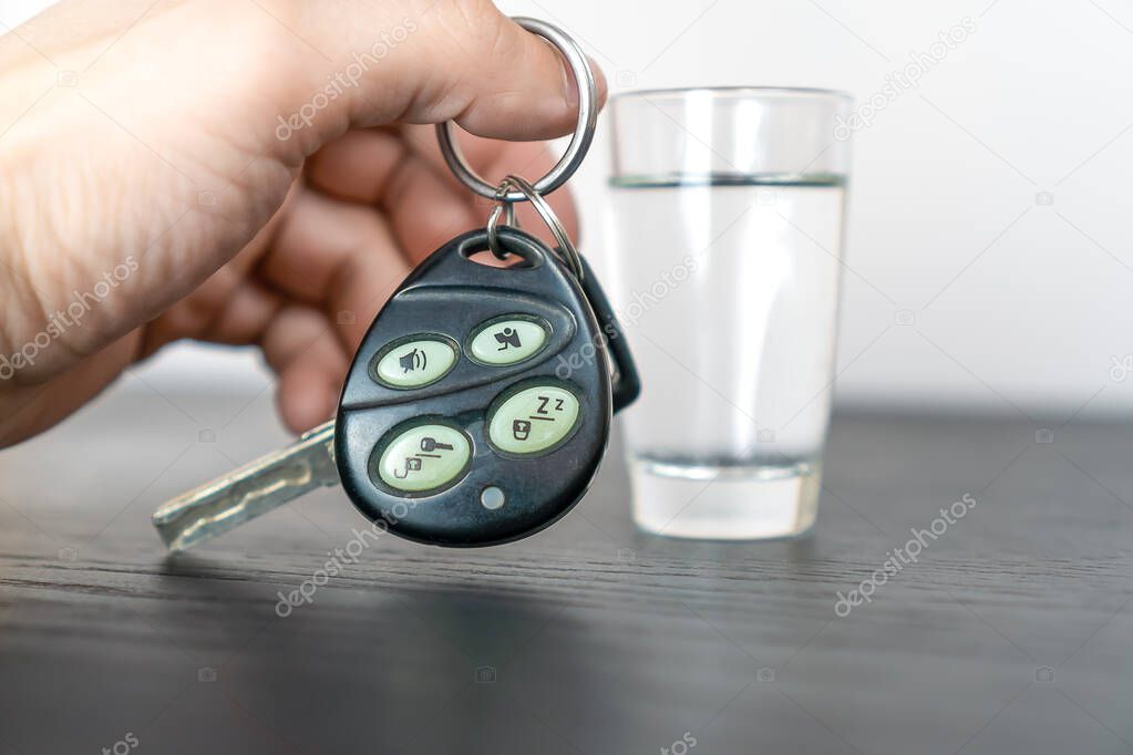 Man's hand takes the car keys and defiantly shows them to the camera against the background of a stack of vodka. Concept of drunk driving