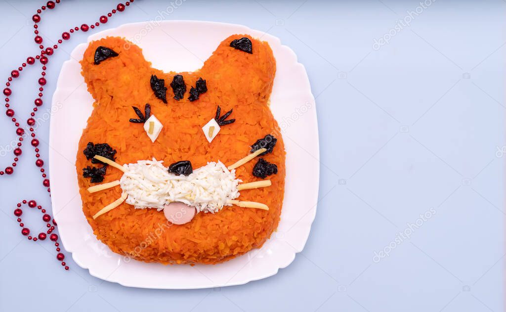 Funny salad in the form of the tiger symbol of 2022, made of carrots, eggs, cucumbers, potatoes, prunes, sausage on a white background.New Year's Christmas food top view,copy space.Holiday,art of food