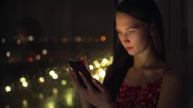 Kız telefonu tutup pencereye bakar ve şehrin arka planına bakar..