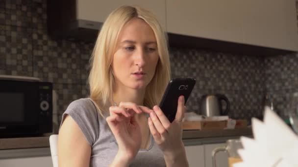 Een mooi meisje zit thuis en gebruikt een smartphone app. — Stockvideo