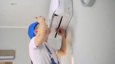 Üniformalı genç bir usta dairedeki klimayı tamir ediyor..