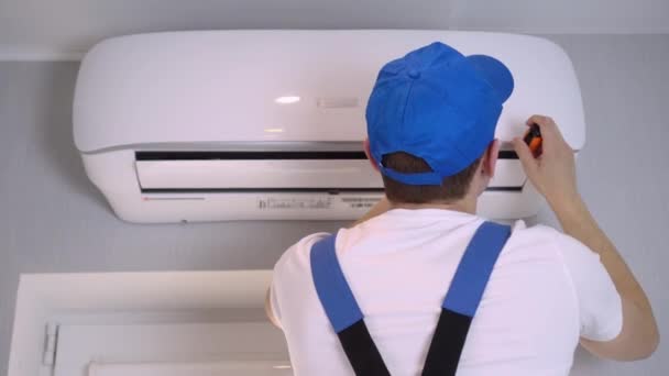 En ung mästare i uniform reparerar luftkonditioneringen i lägenheten. — Stockvideo