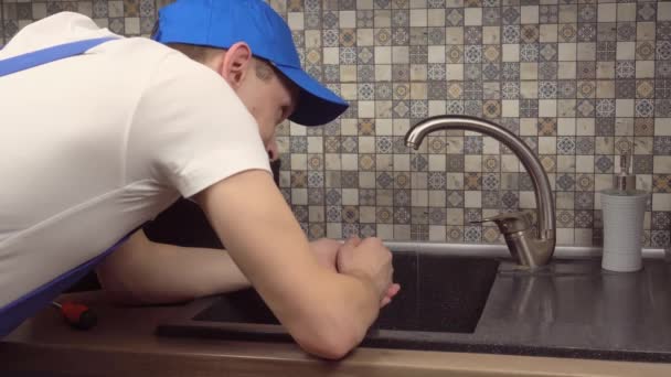 Plombier en combinaison et T-shirt blanc examine le robinet dans la cuisine dans l'appartement. — Video