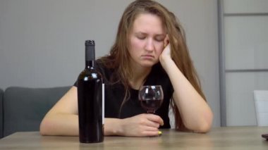Kadın üzgün ve harap bir alkolik. Kanepede oturmuş kırmızı şarap içiyor.