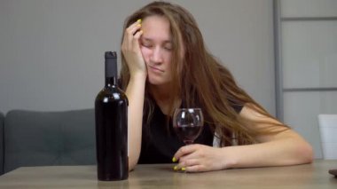 Kadın üzgün ve harap bir alkolik. Kanepede oturmuş kırmızı şarap içiyor.