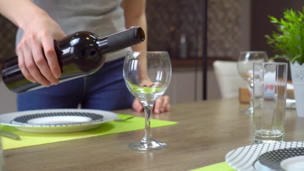 Frauenhände gießen Rotwein in ein Glas auf dem Esstisch in der Küche. — Stockvideo