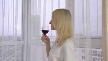 Güzel bir kız bir bardak şarap tutuyor ve pencereden dışarı bakıyor. Şarap tatma..