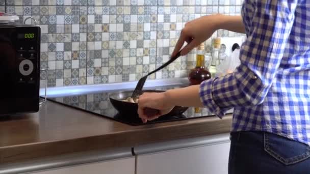 Uma mulher cozinha o jantar em uma frigideira em uma cozinha moderna em casa. — Vídeo de Stock