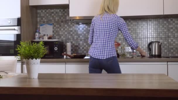 A woman cooks dinner in a frying pan in a modern kitchen at home. — Stock Video