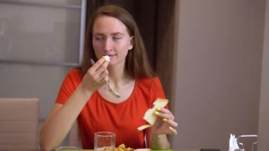 Kırmızı bluzlu genç bir kadın evde masada oturuyor ve beyaz ekmek yiyor..