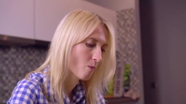 Mutfakta otururken bir kadının yüzü çatalla bilinmeyen bir yemeği yiyor..