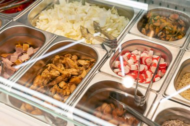 Salataların kendi kendine montajı için hazır malzemeler metal kaplarda, maşayla yakın plan. Dükkanda self servis.