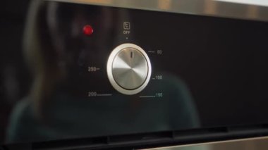 Mutfaktaki elektrikli fırını ayarlayan bir kadın eli.,