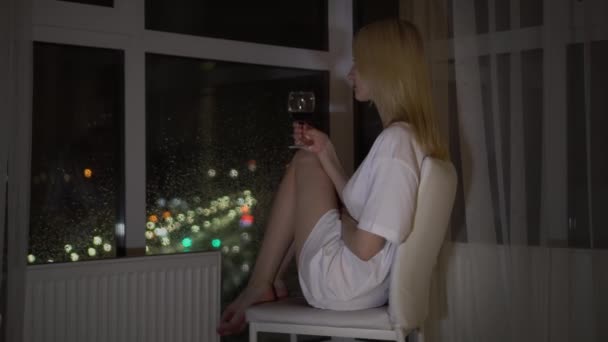 Sobre el fondo de la ciudad nocturna, una mujer sostiene una copa de vino. — Vídeo de stock