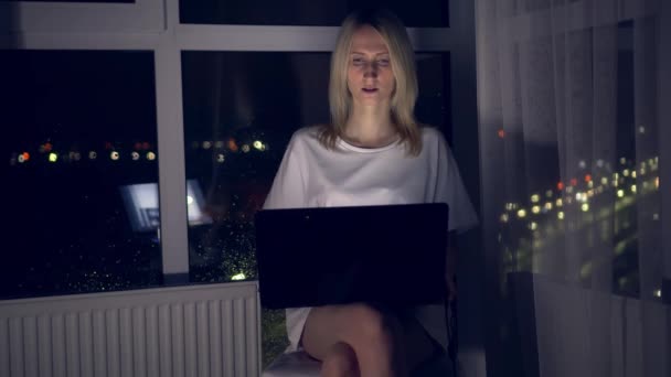 Mladá krásná blondýna sedí u okna a pracuje na notebooku. — Stock video