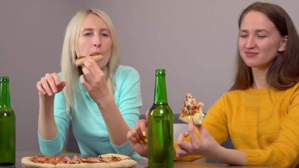 Deux meilleures petites amies heureuses à la maison dans la cuisine manger de la pizza et boire de la bière. — Video