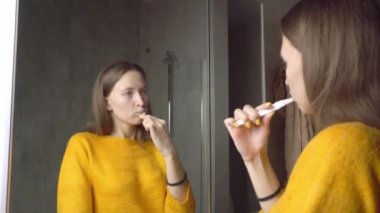 Güzel bir kadının sabah dişlerini aynanın önünde fırçalaması.