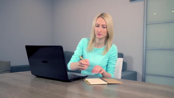 En kvinna jobbar hemma på en bärbar dator. antecknar i en anteckningsbok — Stockvideo