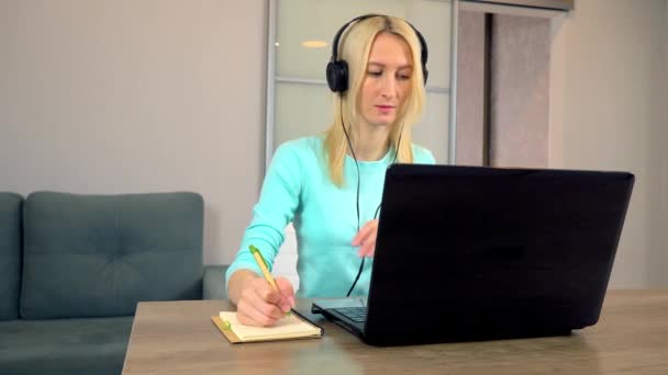 Žena na volné noze se sluchátky mluví ve video chatu pomocí notebooku. — Stock video