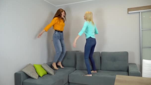 Mujeres con el pelo claro y oscuro saltar juntos en un sofá grande en la sala de estar. — Vídeos de Stock