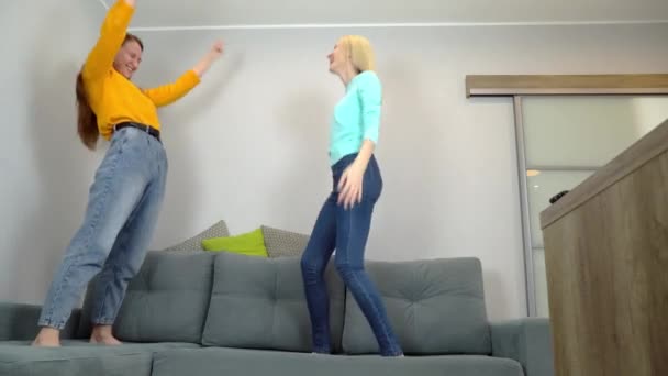 Wanita dengan rambut terang dan gelap melompat bersama-sama di sofa besar di ruang tamu. — Stok Video
