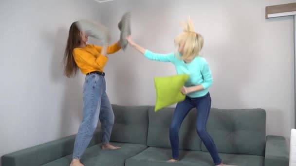 Двое друзей или сестер дерутся с подушками, прыгают на диване дома. — стоковое видео