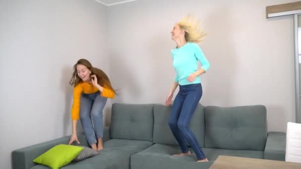 Dos amigos o hermanas pelean con almohadas, saltando en el sofá en casa. — Vídeos de Stock