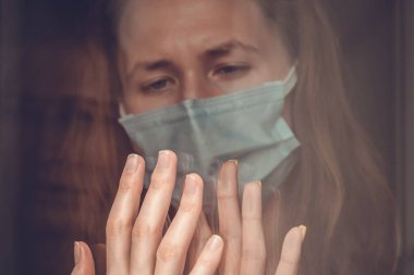 Koronavirüs izolasyonu. Maskeli bahtsız siyah saçlı kız, karantina sırasında cam kapıdan bir kadının eline dokunuyor. Sosyal uzaklık