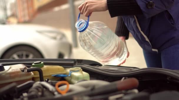 Open de kap van een auto met een vrouw, ze giet water voor de glazenwasser. — Stockvideo