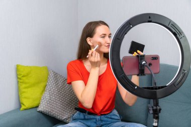 Genç, neşeli, güzel, koyu renk saçlı kadın kozmetik hakkında bir video kaydediyor ya da cep telefonu kamerasında bir güzel akışı yönetiyor.