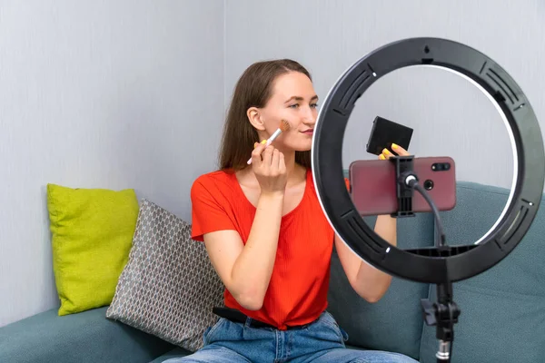 Genç, neşeli, güzel, koyu renk saçlı kadın kozmetik hakkında bir video kaydediyor ya da cep telefonu kamerasında bir güzel akışı yönetiyor.