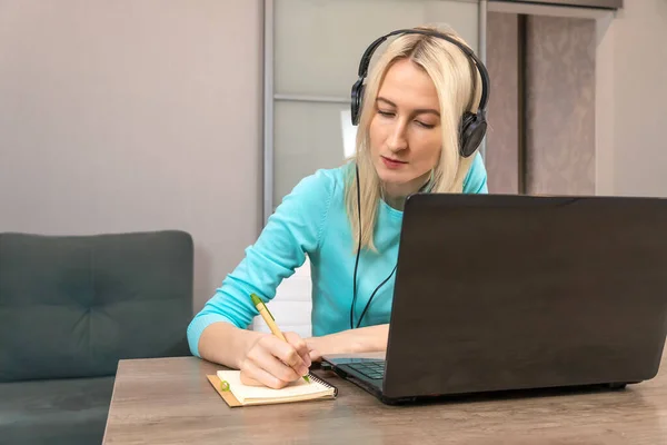 Młoda Blondynka Siedząca Przy Biurku Dużymi Słuchawkami Laptopie Trzymająca Długopis — Zdjęcie stockowe