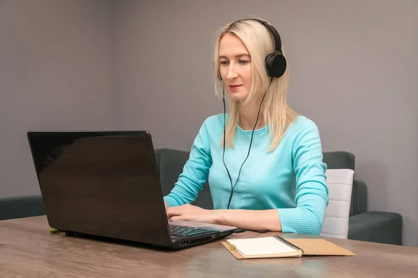 Młoda Blondynka Siedząca Przy Biurku Dużych Słuchawkach Laptopie Słuchająca Wykładu — Zdjęcie stockowe