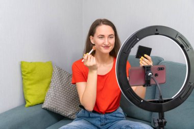 Genç, neşeli, güzel, koyu renk saçlı kadın kozmetik hakkında bir video kaydediyor ya da cep telefonu kamerasında bir güzel akışı yönetiyor.