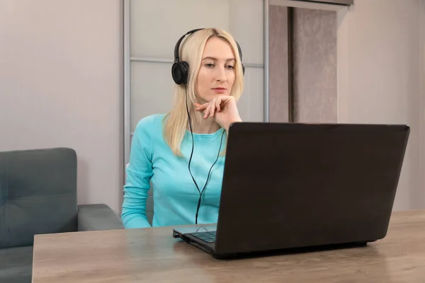 Młoda Blondynka Słuchawkami Siedzi Przy Biurku Patrzy Laptopa Uważnie Słucha — Zdjęcie stockowe