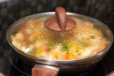 Dilimler halinde beyaz et, çeşitli sebzeler yakın çekim sobanın kapağının altında kızartma tavasında kızartılır.