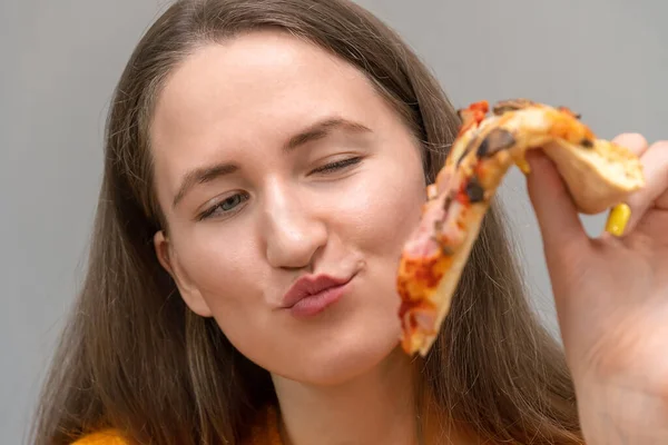 一个漂亮的心满意足的年轻女子的特写镜头 手里拿着一片披萨 凝视着它 充满敬慕之情 把重点放在女人身上 — 图库照片
