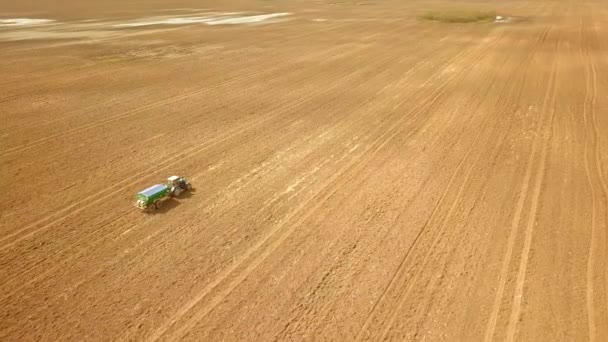 Sett fra luften fra en landbrukstraktor som sprøyter et jorde med gjødsel. – stockvideo