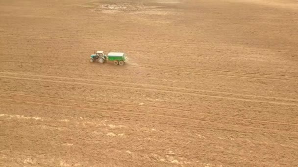 Sett fra luften fra en landbrukstraktor som sprøyter et jorde med gjødsel. – stockvideo