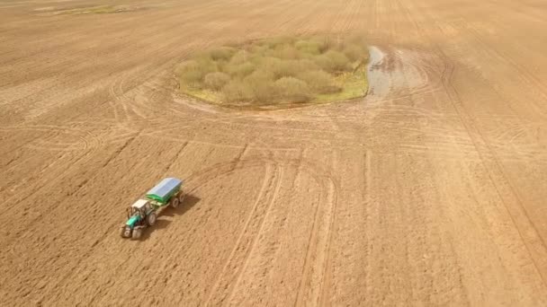 A red old tractor fertilizes a green field in spring — Stock Video