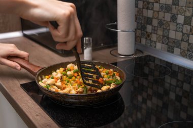 Kadınların elleri bir spatula beyaz et parçasıyla karıştırılıyor, yakın çekimde kızartma tavasında kızartılmış çeşitli sebzeler..