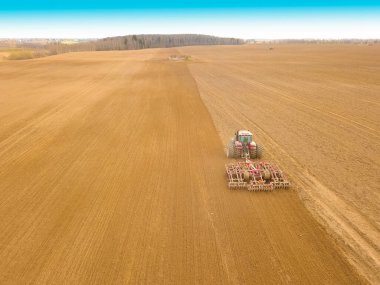 Kırmızı traktör sürüyor, bir bahar günü mavi gökyüzü olan bir tarla ekiyor. İnsansız hava aracı ile fotoğraf