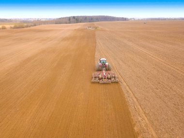 Kırmızı traktör sürüyor, bir bahar günü mavi gökyüzü olan bir tarla ekiyor. İnsansız hava aracı ile fotoğraf