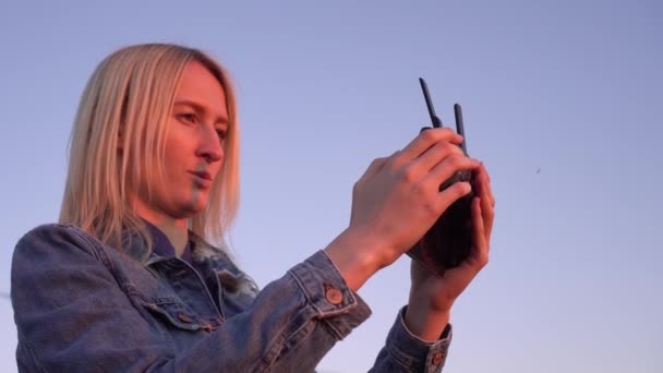 Egy nő kezében van egy távirányító egy drónnak napnyugtakor közelről.. — Stock videók