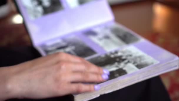 Νεαρή γυναίκα κοιτάζει μέσα από το οικογενειακό άλμπουμ με παλιές ασπρόμαυρες φωτογραφίες — Αρχείο Βίντεο