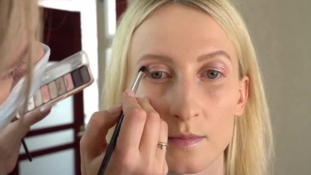 Stylist-makeup artist master applies eye shadow to a young model — Stock Video
